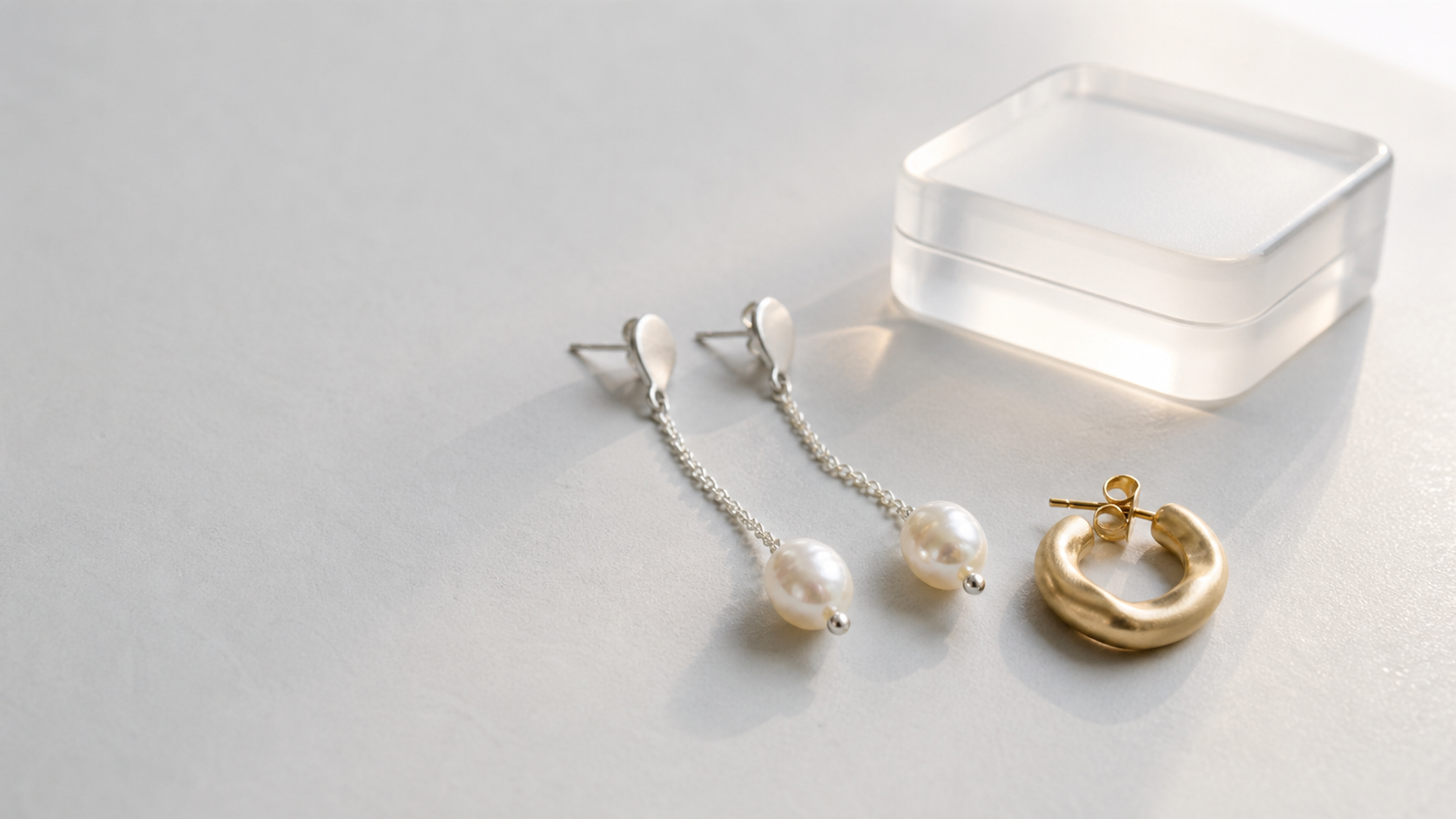 Freshwater pearl drop earrings and a sculptural gold hoop on a pale studio table